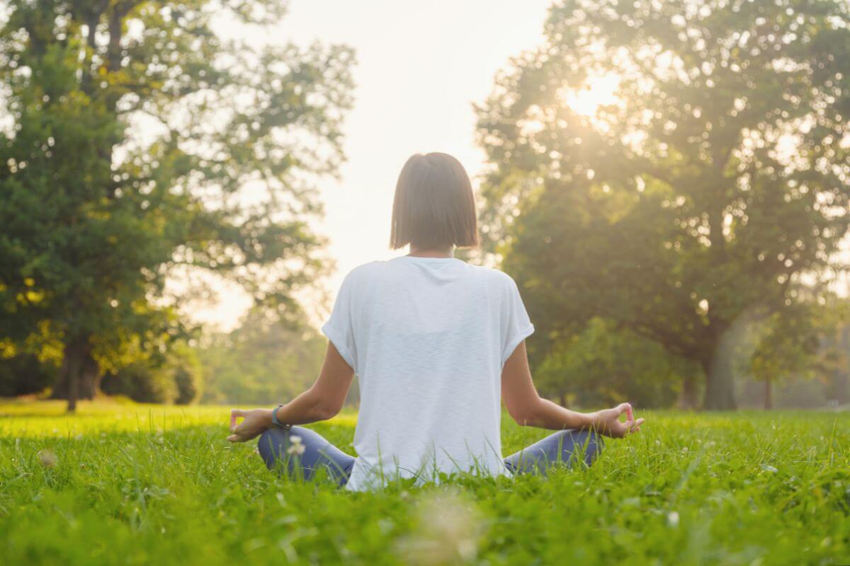 Ratgeber Frau praktiziert Yoga entspannt auf einer grünen Wiese im Freien.