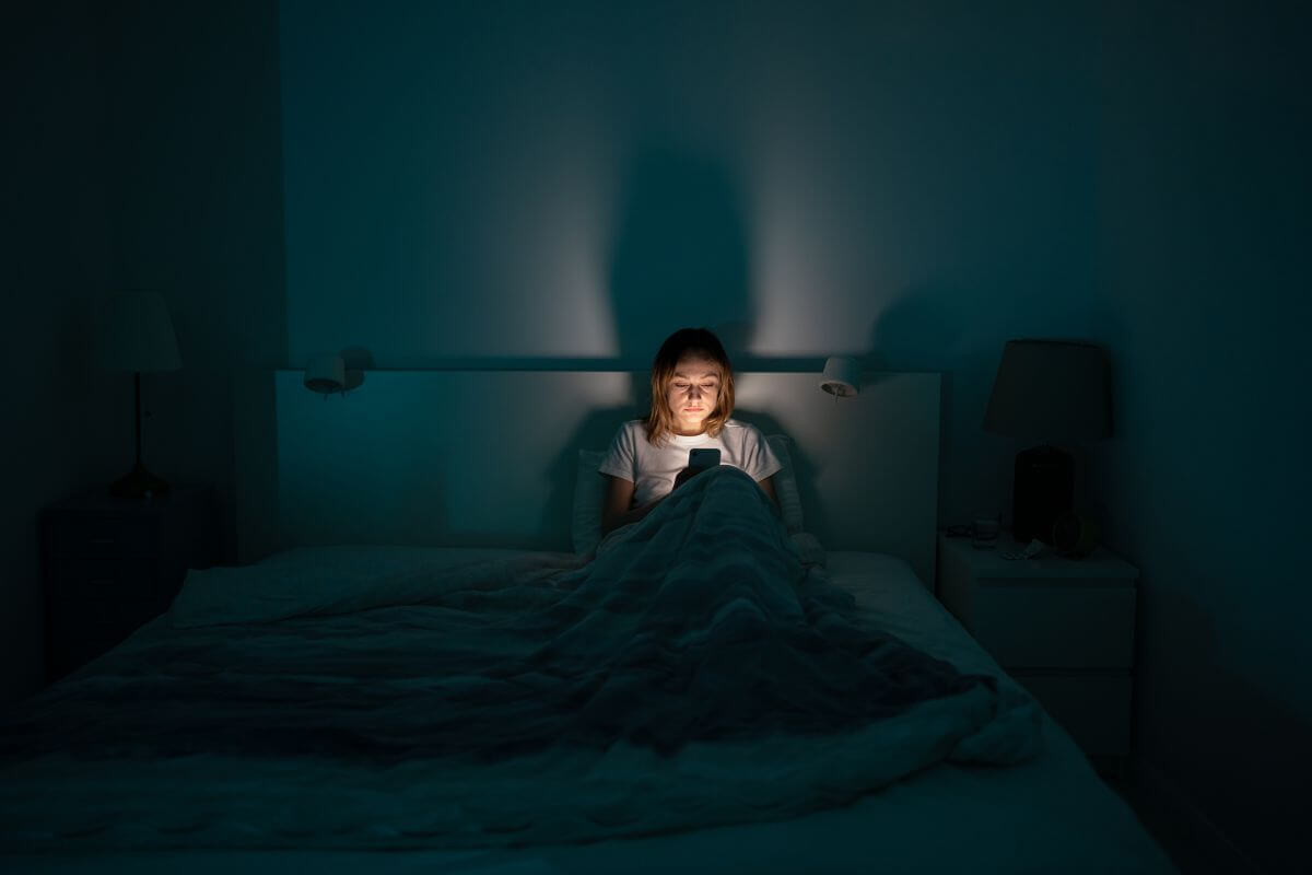 Eine Frau sitzt nachts wach im Bett und schaut auf ihr Handy – typische Situation bei nächtlicher Panik oder innerer Unruhe