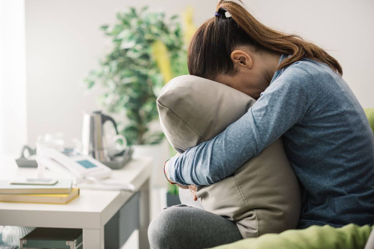 Frau mit Angstzuständen sitzt zusammengerollt auf dem Sofa und sucht Halt – Symbolbild für Angst, Panik und innere Anspannung