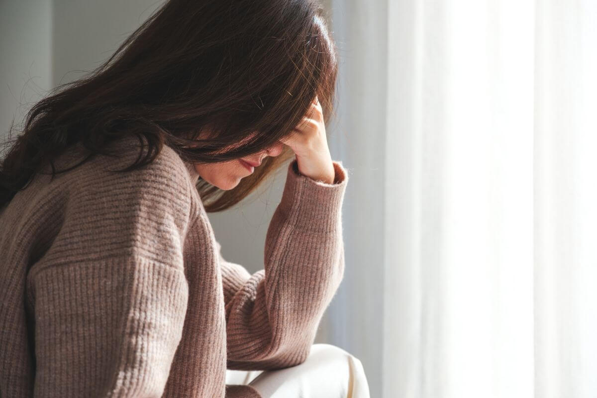 Ratgeber Frau sitzt mit der Hand am Kopf und zeigt typische körperliche Anspannung bei Angst.