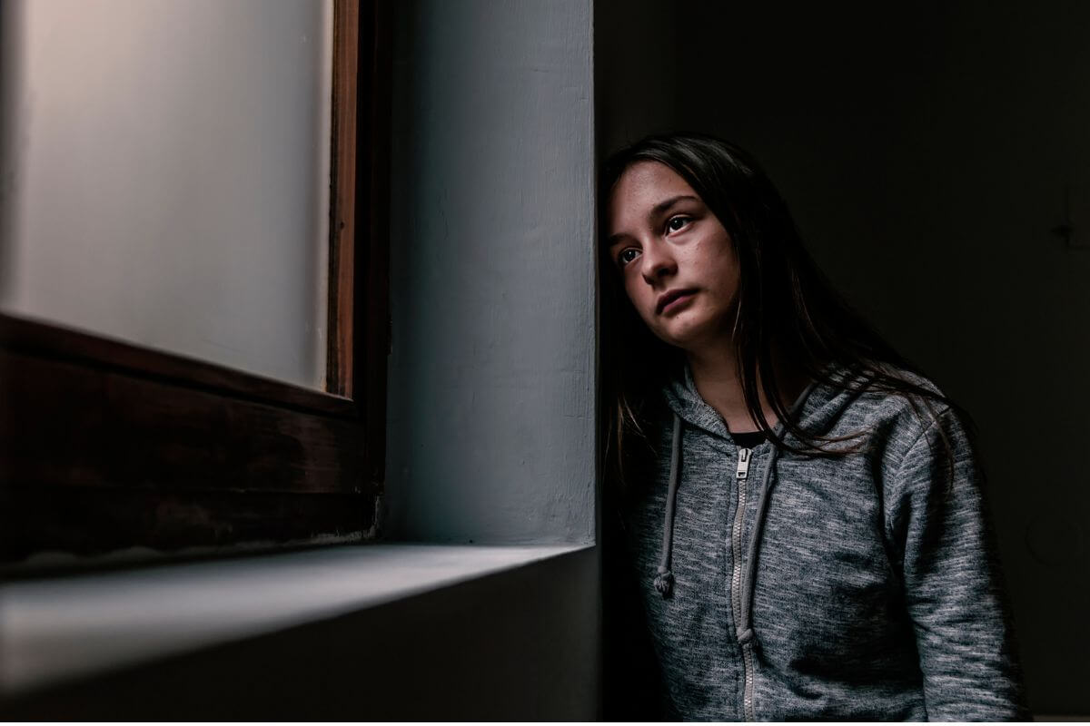 Ratgeber Junge Frau schaut nachdenklich aus dem Fenster – dargestellte innere Belastung und Unsicherheit, ob psychotherapeutische Hilfe benötigt wird.